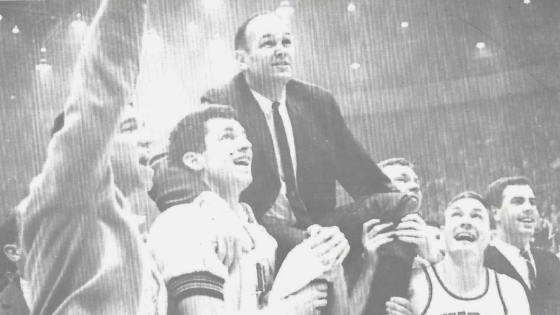 a men's basketball team holds a coach on their shoulders