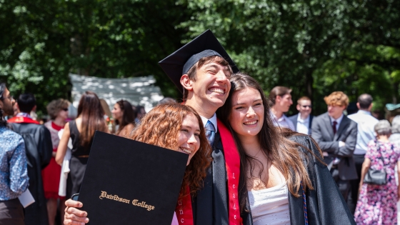 Commencement Three students hugging while getting photo taken, one student is holding his diploma