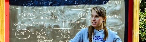 Russian studies TA stands in front of outdoor chalkboard showing writing in Russian