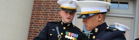 Two ROTC members in formal uniform examine a clipboard while outside