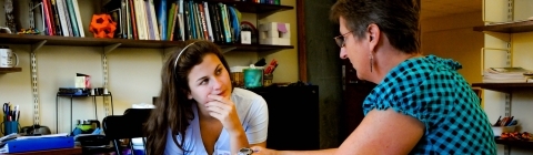 Prof. Molinek sits in her office with student looking at printed materials