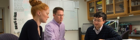 Mark Smith and two students sit around lab table and analyze data