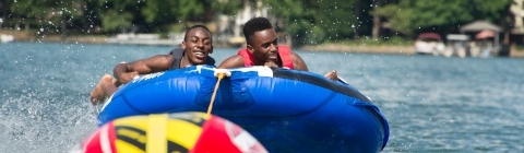 Two kids hang on to a tube as they are pulled across the water, laughing