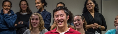 Students are framed through blue gloves of speaker, laughing, with Nail Mamoon in the background