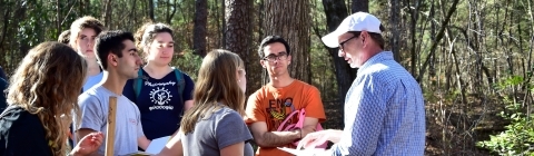 Prof. Dave Backus stands with class in a field explaining a concept