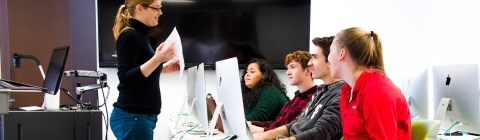 Prof. Peck talks to four students that each use a desktop computer