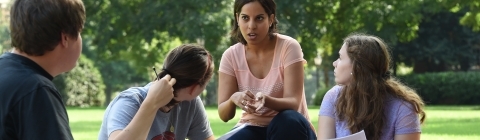 Professor kneals with students while leading class outside