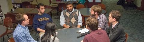 Professor and six students sit around a round table in the Union discussing economics