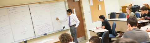 Economics professor writes on board while students take notes