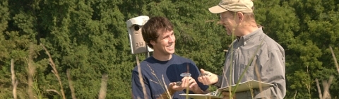 Professor and student hold baby birds at a field nesting habitat