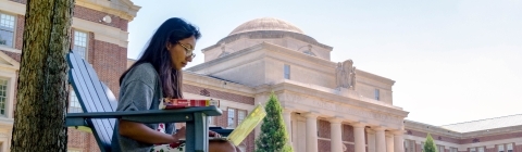 Student sits on outdoor chair on Chambers Lawn and does classwork