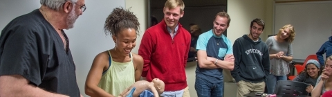 Student participates in a delivery demonstration in the classroom with a doctor while class members gather around and watch