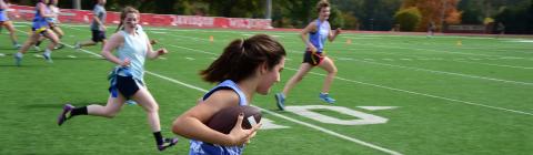 Flickerball game shows a student holding a football under her arm and running while others try to catch up to her