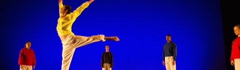 Student leaps into the air in front of blue lights while other dancers on stage stand still