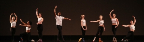 Dancers on stage take different positions in front of a black background