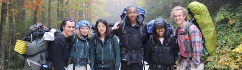 Students backpack with camping gear in the mountains with fall foliage