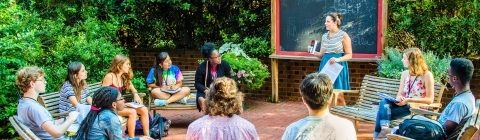 Students sit in a circle in outdoor classroom while listening to professor