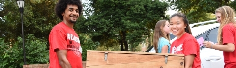 Two students carry a big trunk inside during move in day