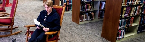 Student Reads Book in Library Rocking Chair