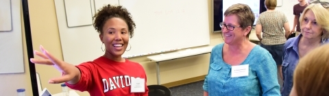 Student stands near screen and points while crowd gathers around her and hears her share