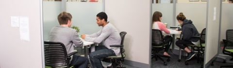 Two sets of students meet in glass cubicles with student writing tutors