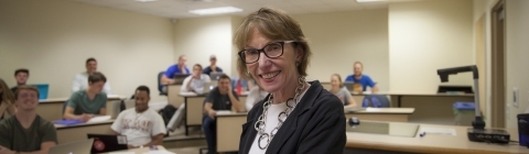 Prof. Roberts smiles at camera while leading class from podium