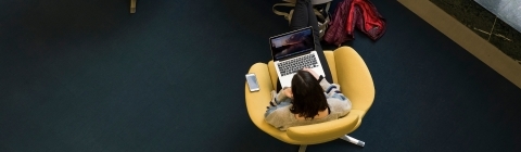 Student sits in yellow, modern chair while on laptop