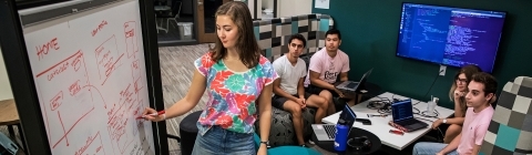 Student writes on board collaborating with a student team