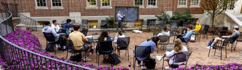 Davidson College Professor Hammurabi Mendes teaches class students outdoors with chalkboard surrounded by purple flower bushes