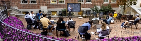 Davidson College Professor Hammurabi Mendes teaches class students outdoors with chalkboard surrounded by purple flower bushes