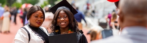 Commencement Ceremony where Graduate Holds Diploma and Hugs Family Member