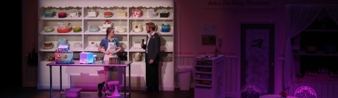 Actress standing in front of a giant display case full of decorative cakes