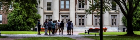 Group of people standing in front of brick building with green trees around