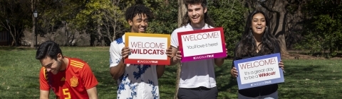 Students holding "welcome" signs and smiling