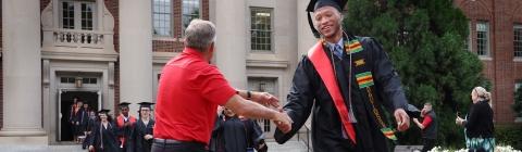 A man shakes hands with a student in graduation robes