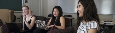 Three students smiling and talking to each other on a couch