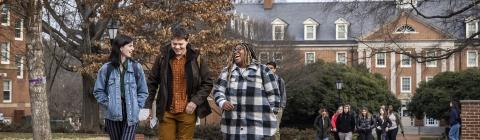 Three students walk together on campus and smile at each other