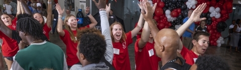 A group of students in red shirts cheer and welcome new students 