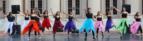 A group of students in colorful outfits dance outside