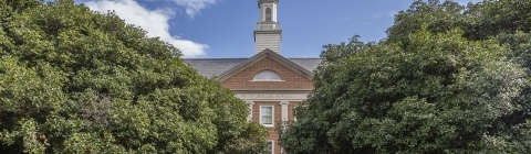 a brick building surrounded by green trees and blue skies in the background