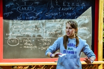 Russian studies TA stands in front of outdoor chalkboard showing writing in Russian