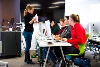 Prof. Peck talks to four students that each use a desktop computer