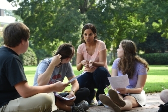 Professor kneals with students while leading class outside