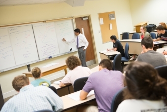 Economics professor writes on board while students take notes