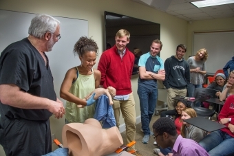 Student participates in a delivery demonstration in the classroom with a doctor while class members gather around and watch