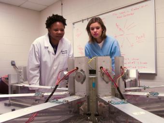 Two students stand in lab coats looking at lab equipment while running an experiment
