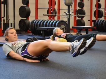 Two students do exercises on a mat inside weight room