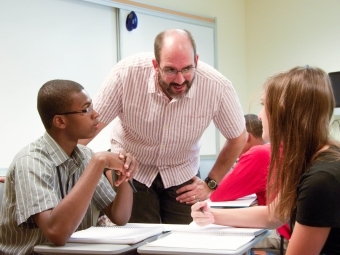 Prof. Marti leans in near two students and joins their discussion