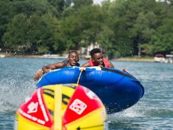 Two kids hang on to a tube as they are pulled across the water, laughing