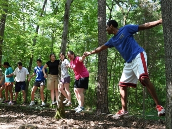 Students hold hands while standing on logs and try to complete a Davidson Outdoors challenge course